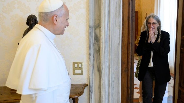 Pope Leo XIV, in profile, smiles at Patti Smith, who waits at the doorway with her hands clasped before her face.